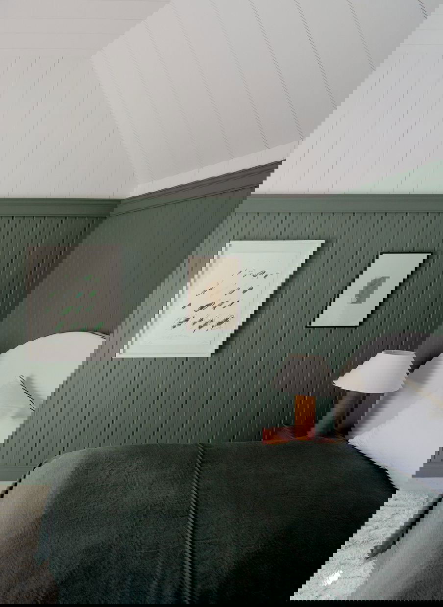 Спальня с тёмно-зелёными деревянными панелями и минималистичным изголовьем: спокойный цвет и простые рамочные картины на стене.