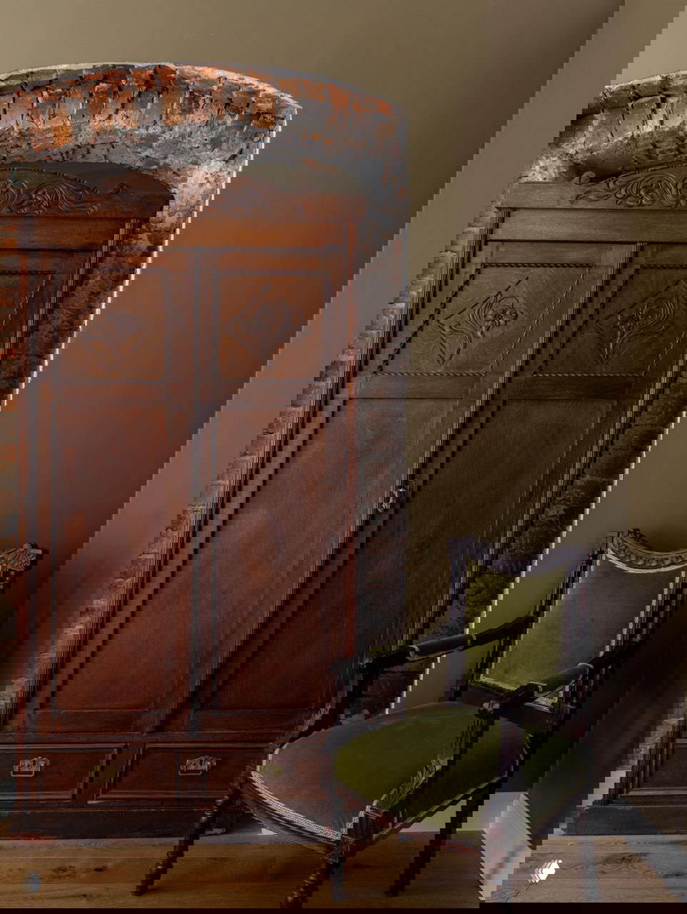 Антикварный деревянный шкаф в нише из старинного кирпича рядом с резным креслом с зелёной обивкой — элементы подлинной мебели XIX века в интерьере отеля.