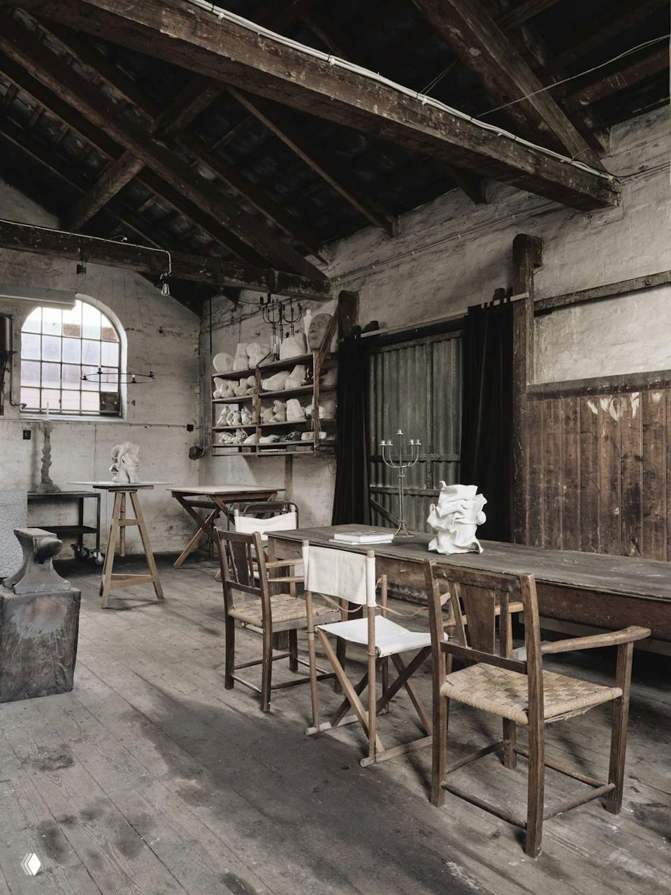 Ателье/мастерская с деревянными столами и стульями, полками со скульптурами и индустриальными элементами — атмосферный рабочий интерьер художника.