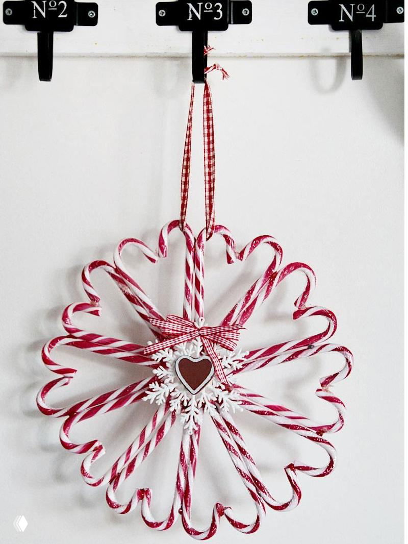 Декоративный венок из леденцовых тростей и красно‑белых конфет, аккуратно подвешенный на крючке в прихожей в праздничной палитре.