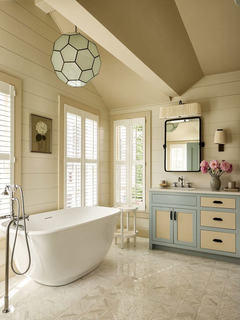 Светлая ванная с отдельной белой ванной, большой окном и тумбой в пастельных тонах — спокойный контраст к насыщенным комнатам дома.