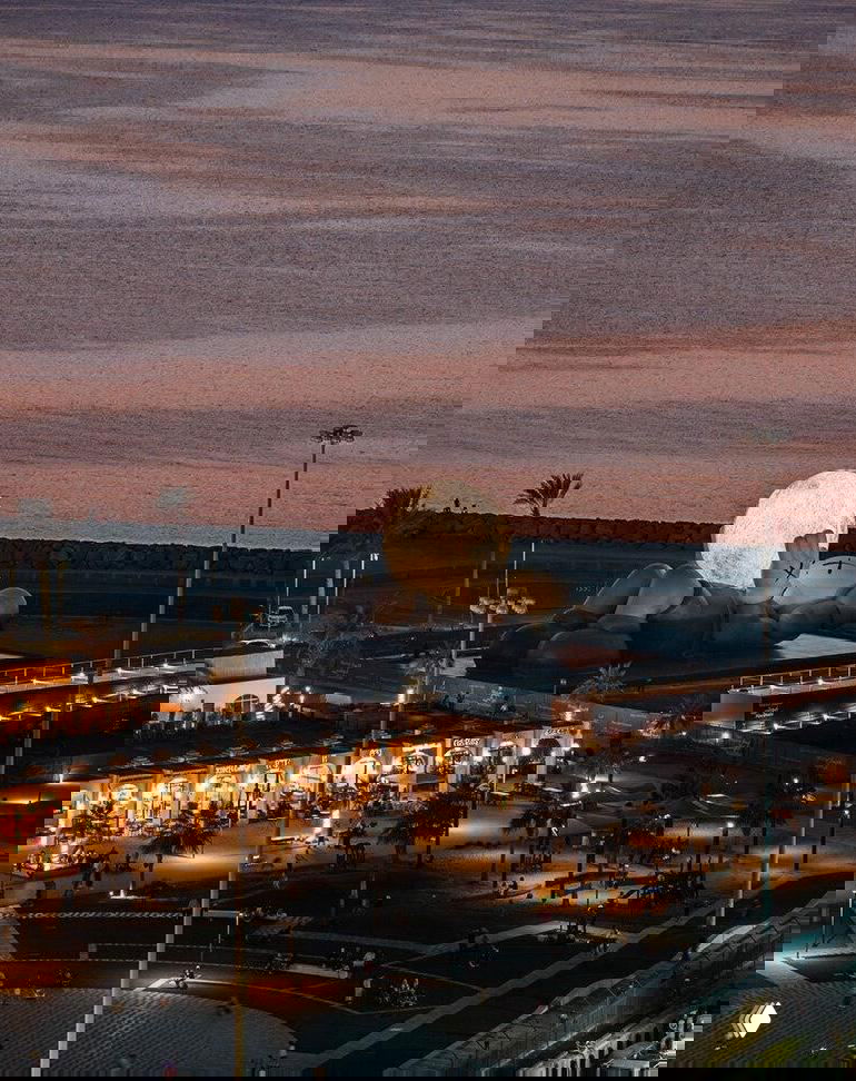 Ночная фотография 32-метровой инсталляции KAWS «Компаньон» на набережной Мина Зайед в Абу-Даби, фигура держит светящуюся луну, вид на залив и огни.