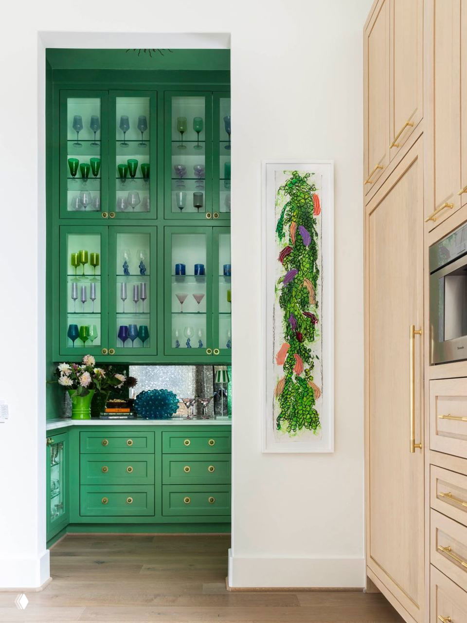 Зелёная буфетная зона: шкафчики насыщенного изумрудного цвета со стеклянными витринами, сервировка и светлая деревянная отделка рядом с кухней.