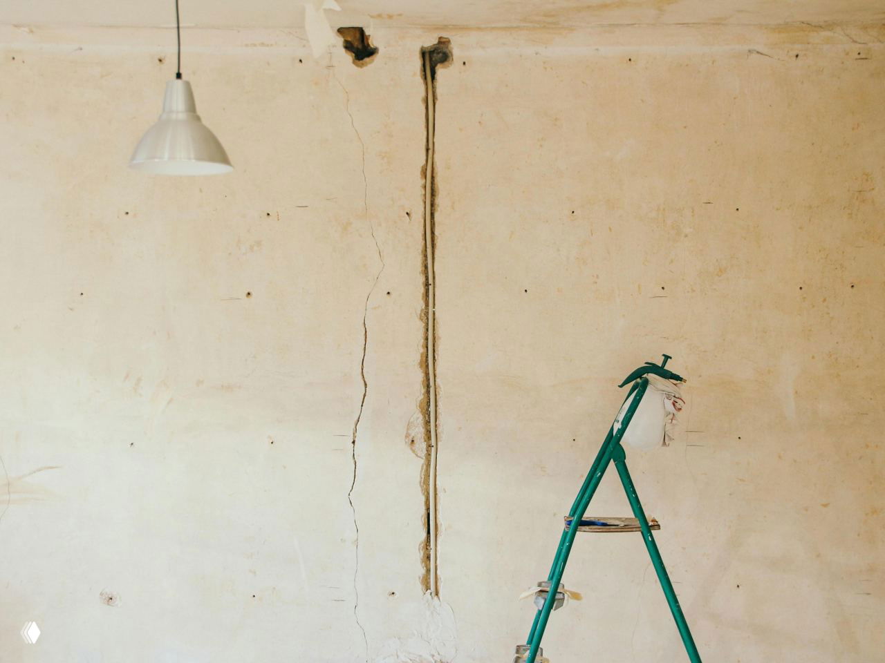 Лестница у оштукатуренной стены с видимой штробой и трещинами в процессе ремонта, подвесной светильник и пустое помещение.