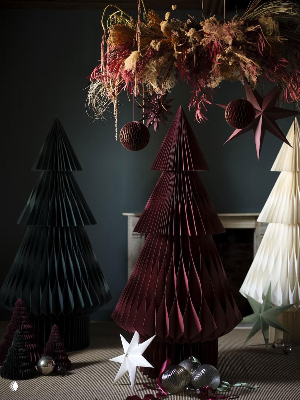 Сцена с декоративными складными бумажными елками тёмно-бордового, чёрного и белого цветов, над ними подвешена сухая цветочная композиция и звёзды.