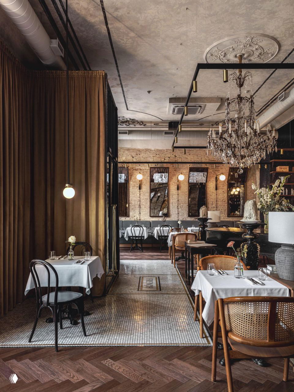 Широкий вид на ресторанный зал: столы со скатертями, коллекция зеркал на стене, хрустальная люстра и мозаичная плитка на проходе.