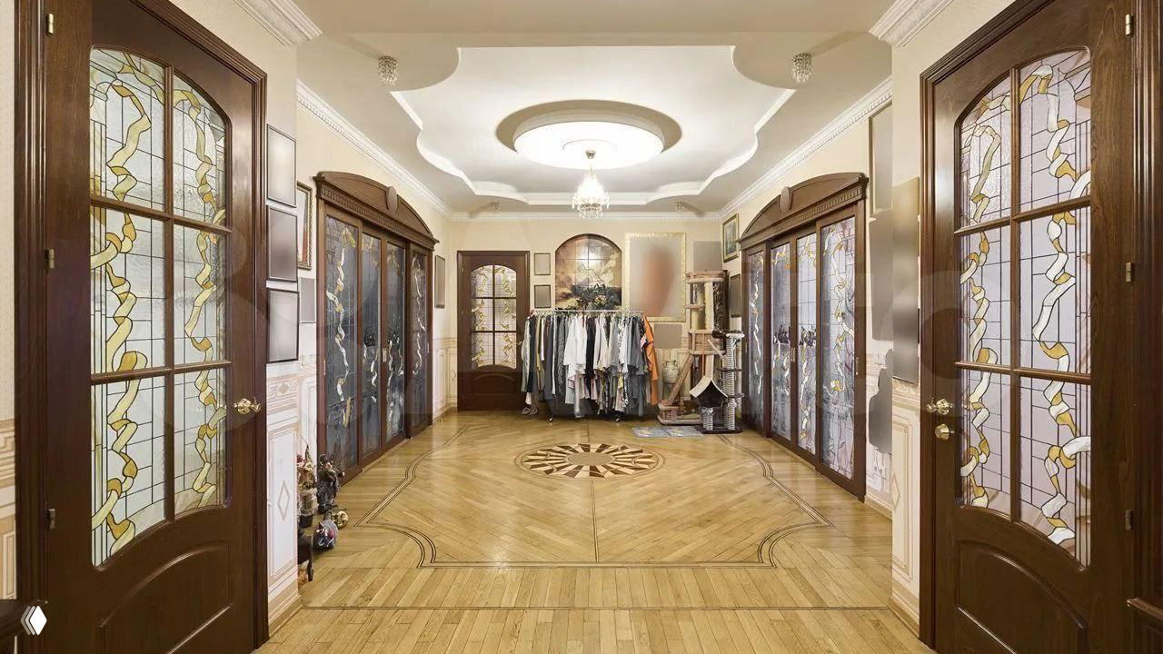 Широкий холл с декоративными витражными дверями, паркетным рисунком на полу, многоуровневым потолком и люстрой в просторной элитной квартире.