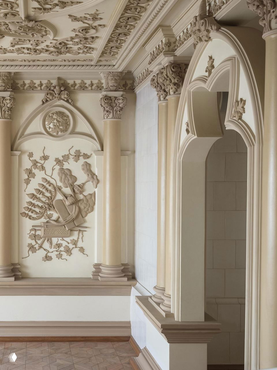 Интерьер усадьбы: колонны и арочная ниша с тонкой лепниной, барельеф с лирой и растительным орнаментом в нежной кремовой гамме и мягком освещении.