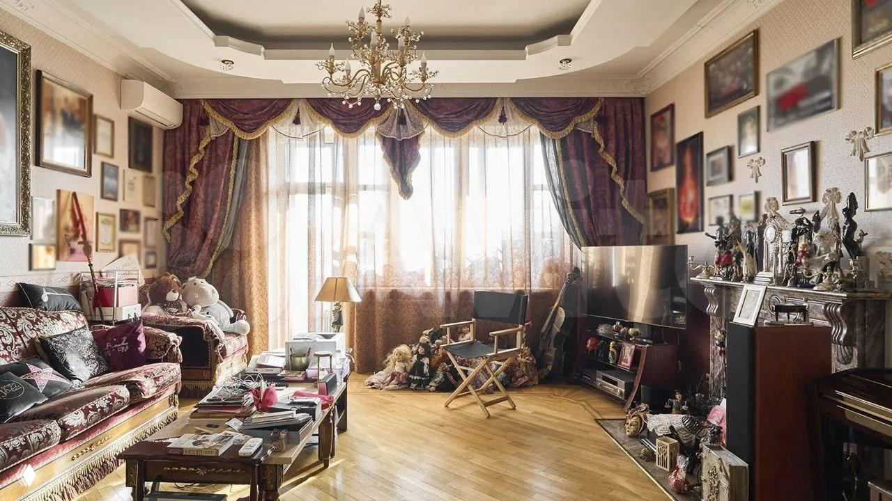 Гостиная с богато украшенными шторами, старинной мебелью, множеством рам и декоративных предметов — плотный классический интерьер с тёплой палитрой.