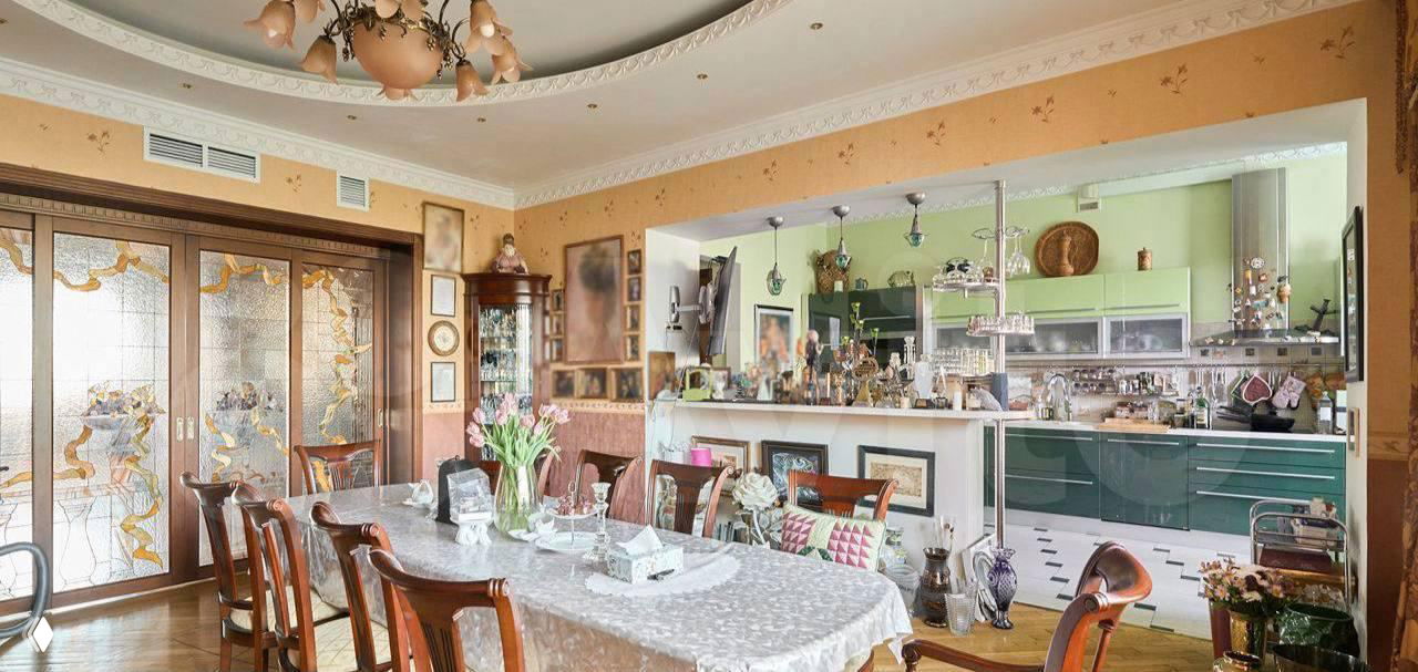 Столовая зона, переходящая в открытую кухню: стол с покрывалом, декоративные элементы и витражные раздвижные двери, интерьер сочетает классику и современные элементы.