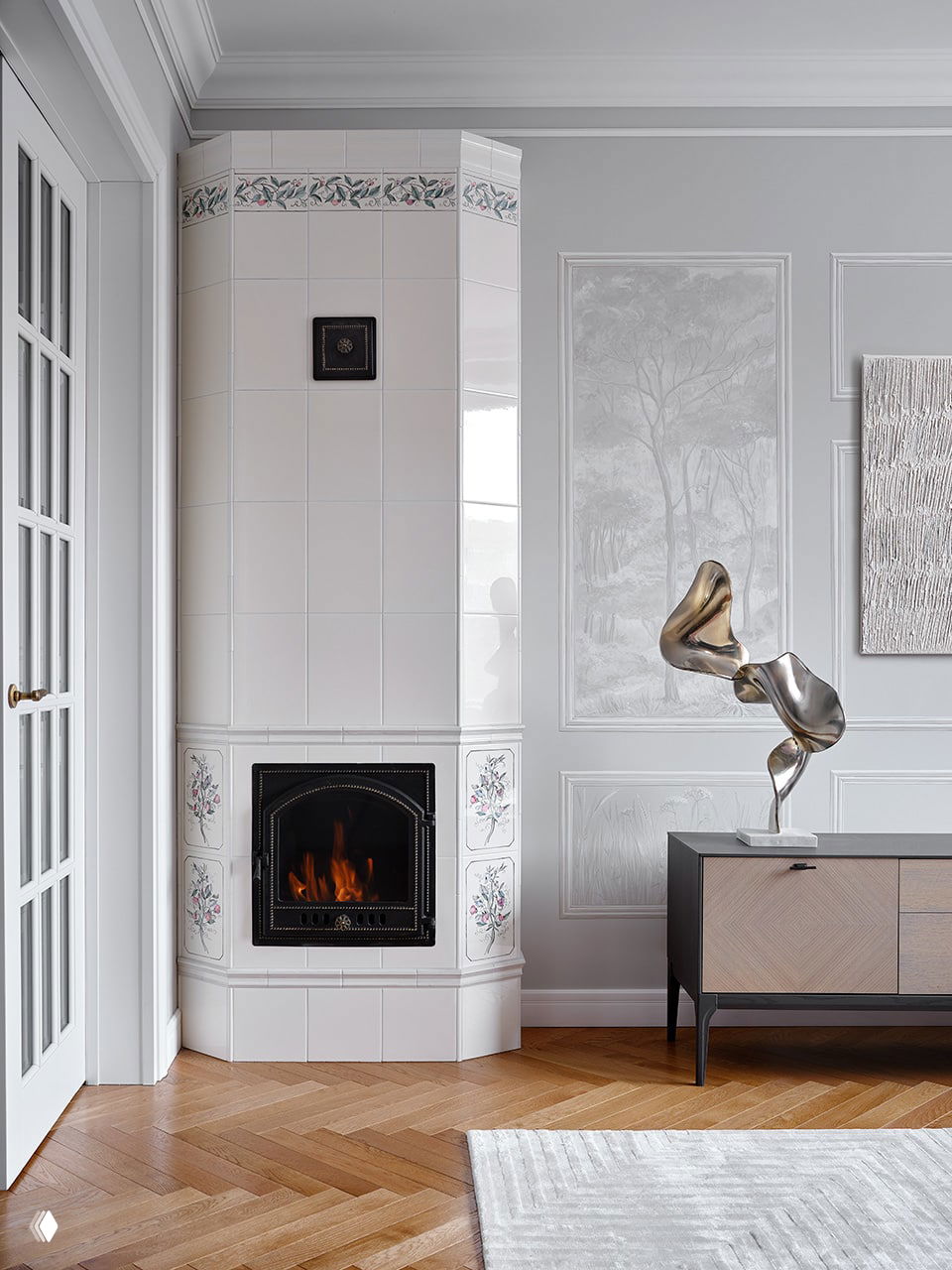 Классическая белая печка-камин с цветочным декором на плитке, рядом настенная роспись, скульптура и элегантный комод в комнате.