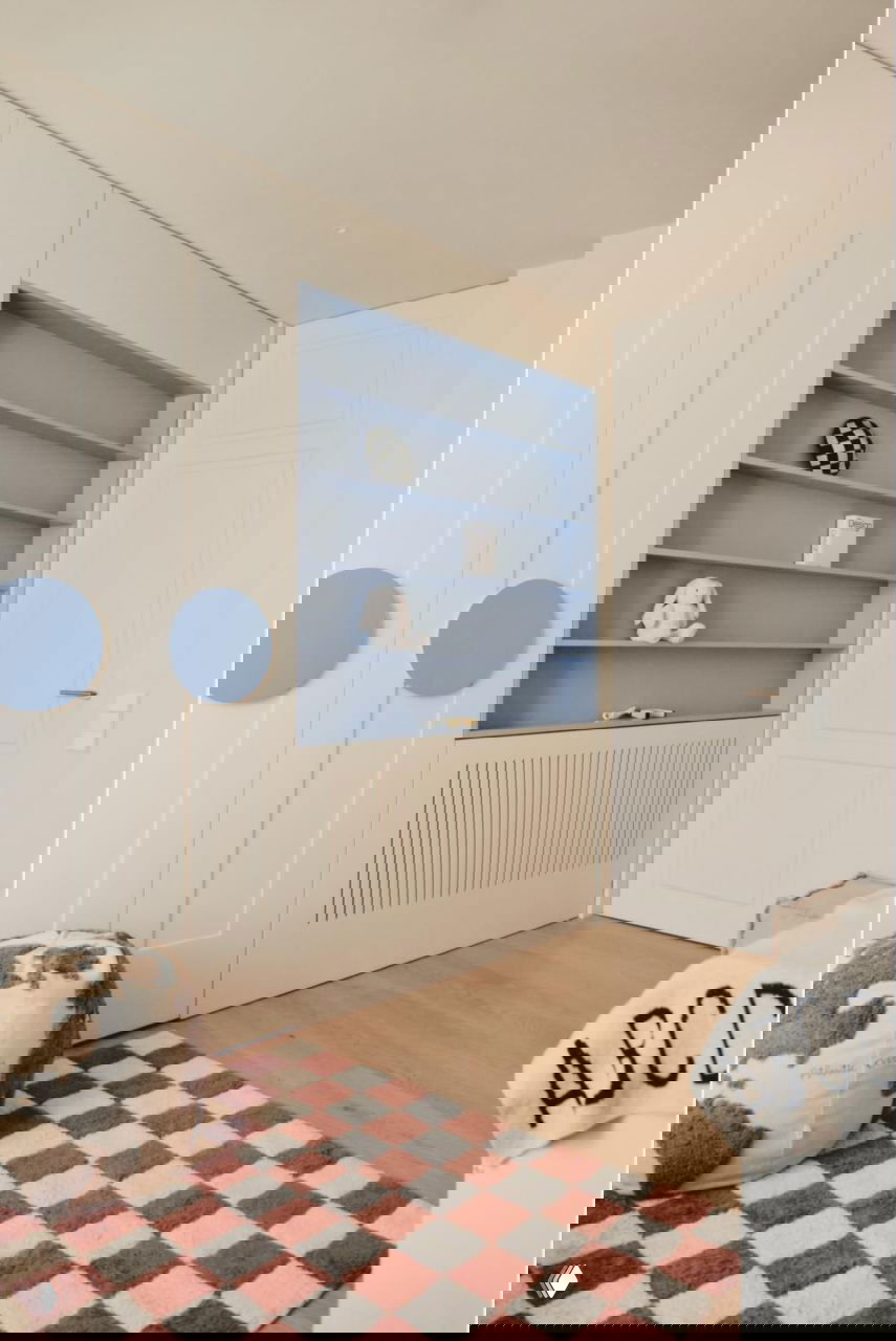 Детская или кабинет с встроенными шкафами, голубыми нишами для хранения, мягким пуфом и клетчатым ковриком на деревянном полу.