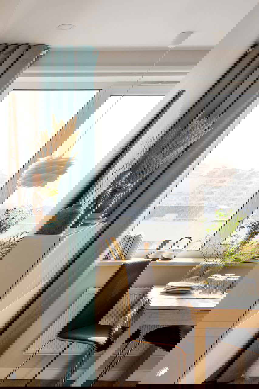 Обеденная зона у большого окна: стол, стул и подоконник с книгами и растениями, видна городская застройка за окном квартиры в Петербурге.