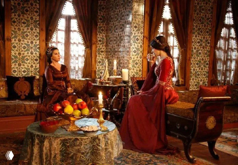 Кадр с героиней у низкого стола, на котором сервировано блюдо и свеча; в комнате много текстиля и декоративных предметов эпохи воссоздания.