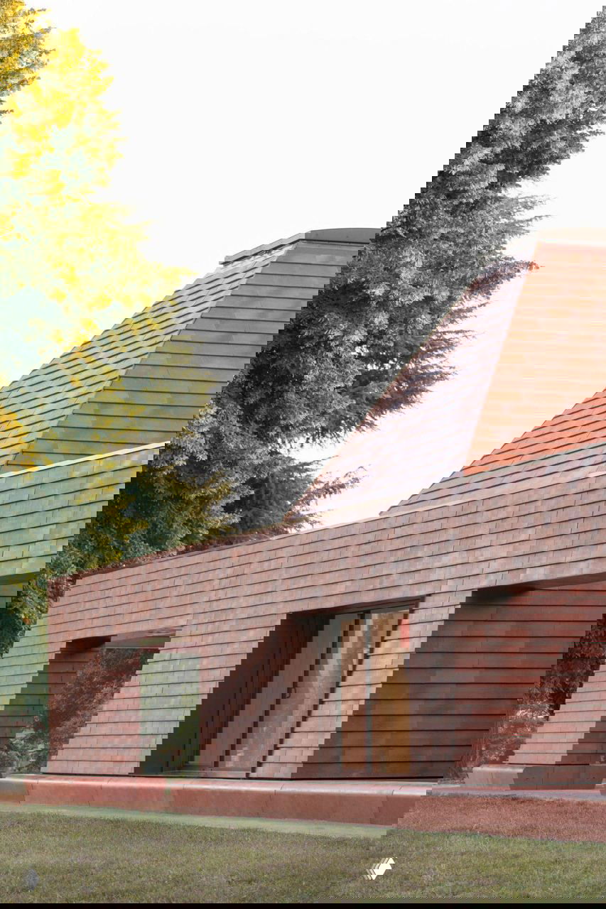 Ряд пирамидальных «домиков» детсада в терракотовой гамме, окна и проёмы смотрят на зелёный сад, подчёркивая модульную композицию здания