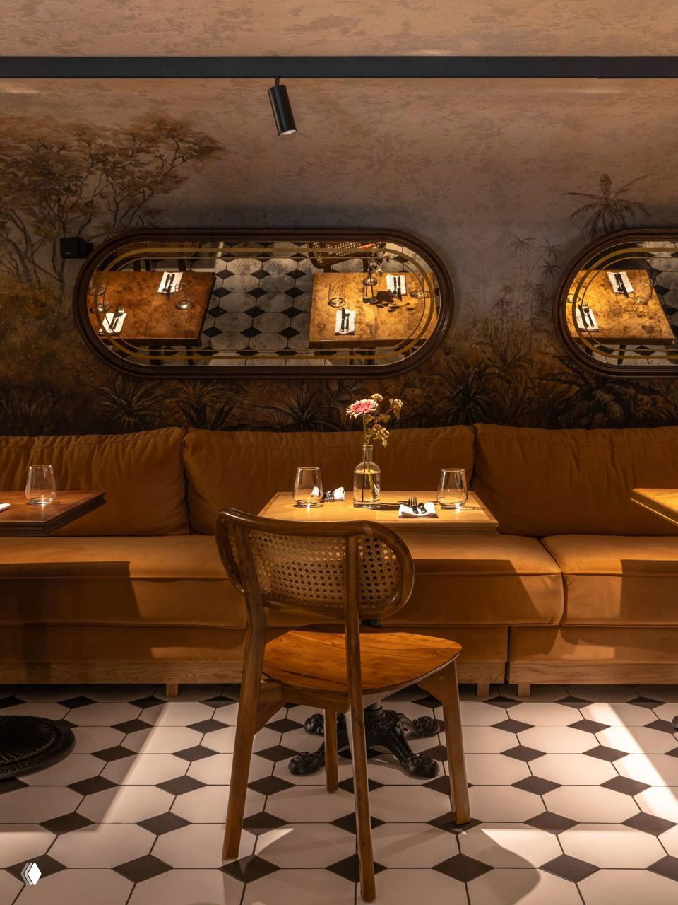 Камерная обеденная зона с настенной росписью в нейтральных тонах, мягкие диваны, деревянные столы и плитка в шахматный узор на полу.