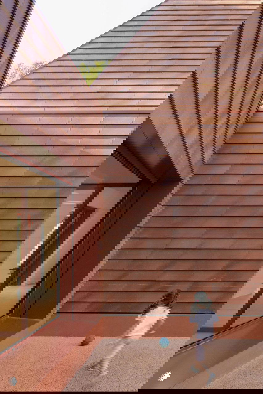 Фасад с крупными прямоугольными проёмами и ступенчатой базой, терракотовые панели образуют ровную ритмичную поверхность на уровне улицы