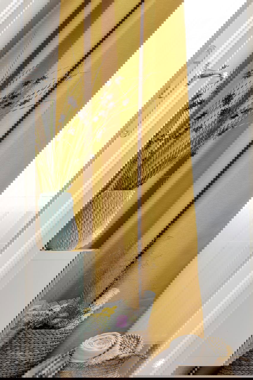 Деталь интерьера: декоративные жёлтые шторы и плетёная корзина с текстилем и растениями, создающие тёплый акцент в нейтральной палитре.