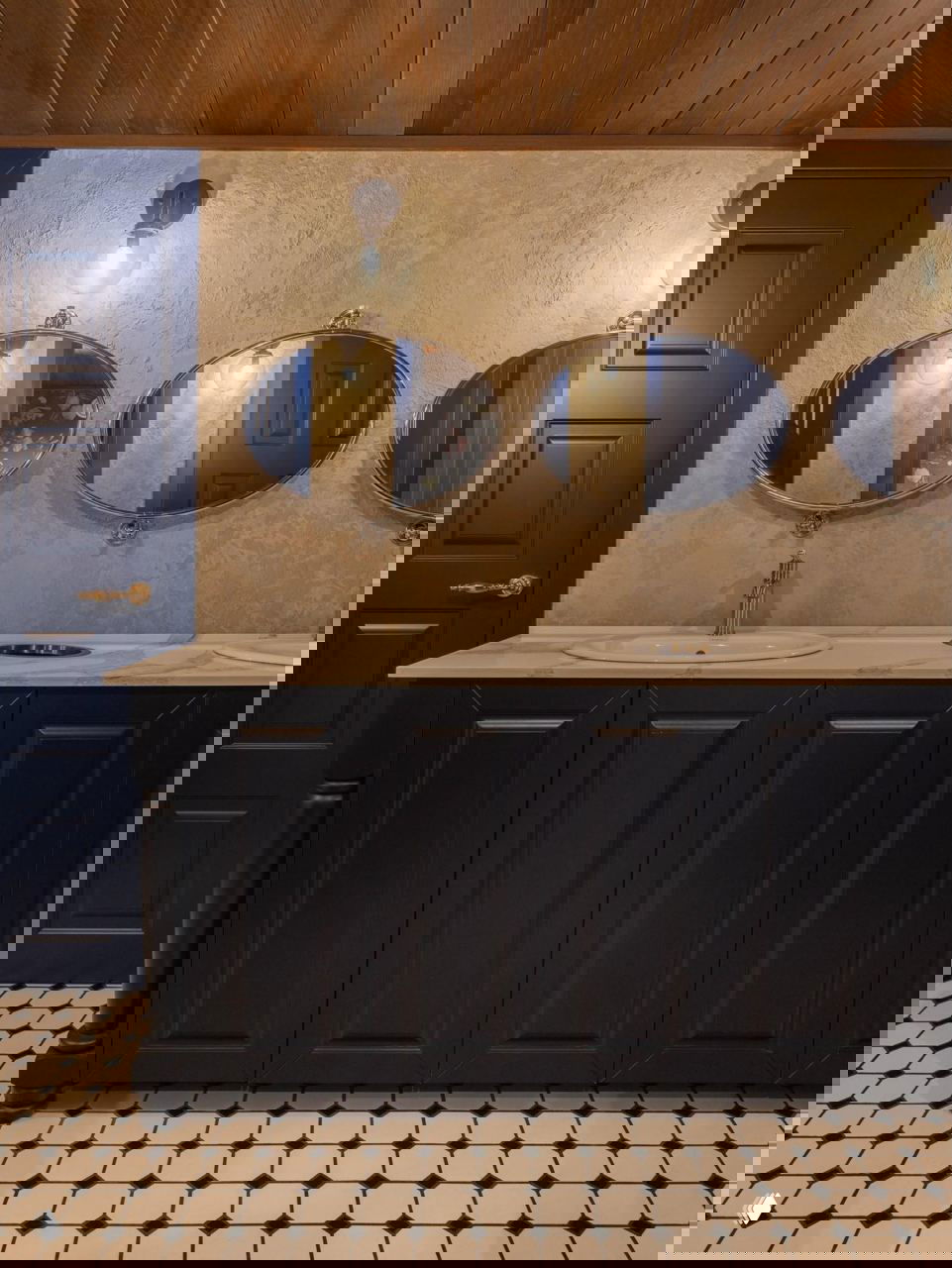 Туалетная зона и умывальники с тремя овальными зеркалами, темно‑синей мебелью и мраморной столешницей на фоне чёрно‑белой плитки пола.