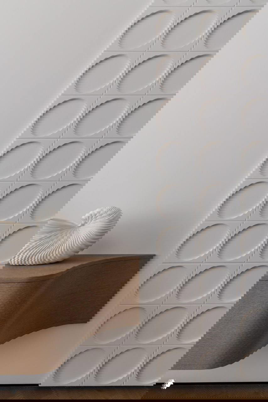 Фрагмент стены с круглыми рельефными плитками и деревянная консоль-накладка — сочетание текстур и мягких белых оттенков в интерьере.