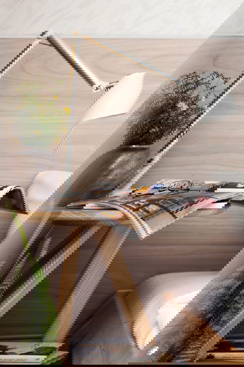 Близкий план прикроватного столика: лампа, журнал, очки и керамическая ваза с зеленью — пример функционального мелкого декора в небольшом пространстве.