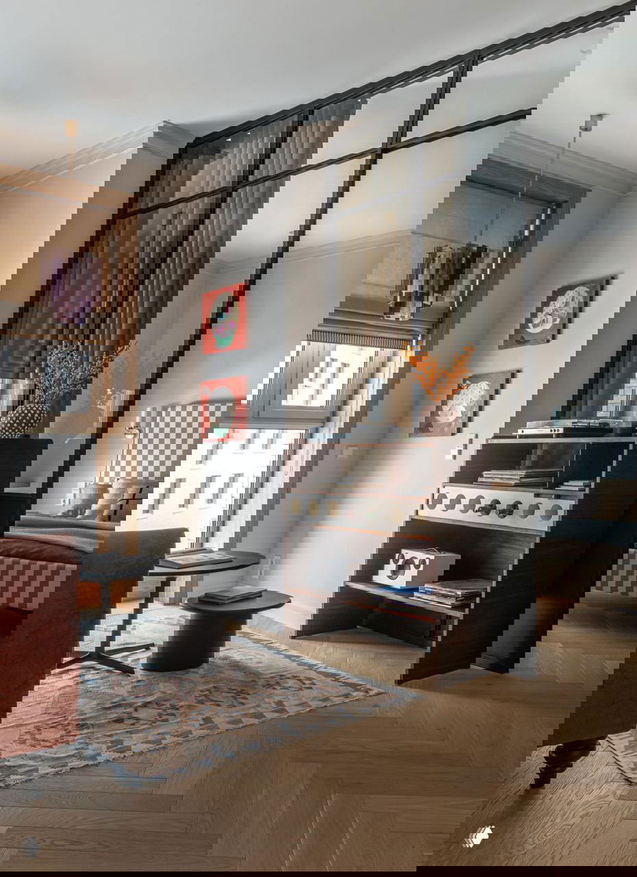 Угол гостиной с полкой-баром из темного дерева, виниловым проигрывателем и стеклянной перегородкой, отделяющей спальню от общей зоны.