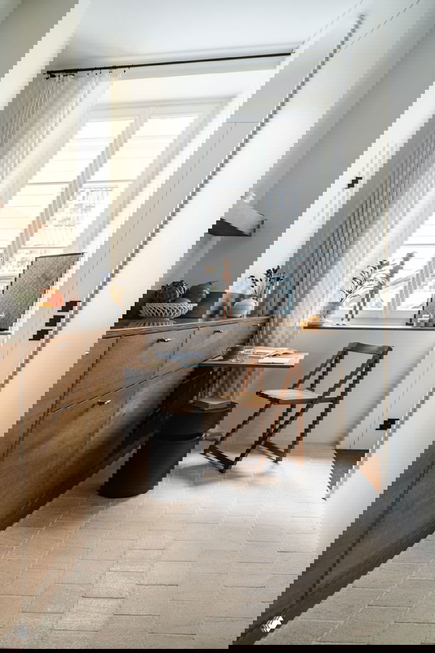 Рабочее место у окна в маленькой квартире: складной стол, простой деревянный стул и светлый текстиль на фоне большого окна.