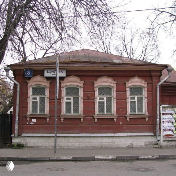 Невысокий деревянный дом в традиционном стиле с табличкой «Щипок» на углу; фасад, деревянные наличники и городской тротуар на переднем плане.