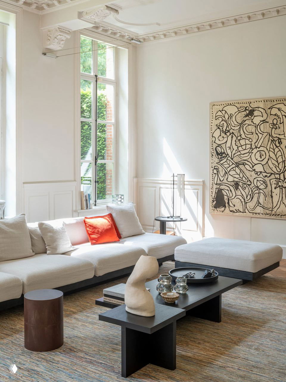 Светлая гостиная в замке Бергейк с большой белой модульной софой, низким черным кофейным столом и декором в виде скульптур и посуды.