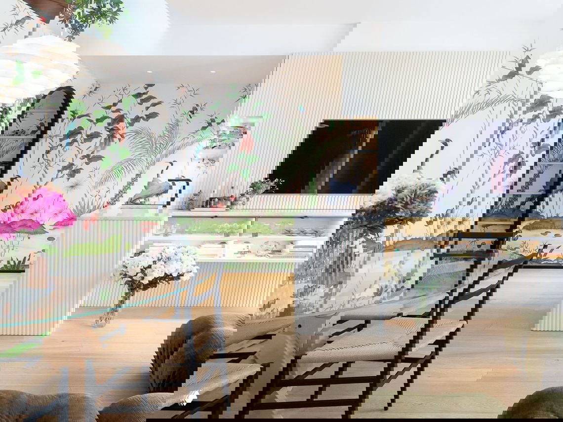 Гостиная-столовая дуплекса в Милане: стеклянный обеденный стол, черные стулья и раскрашенные обои с птицами и растениями на стене.