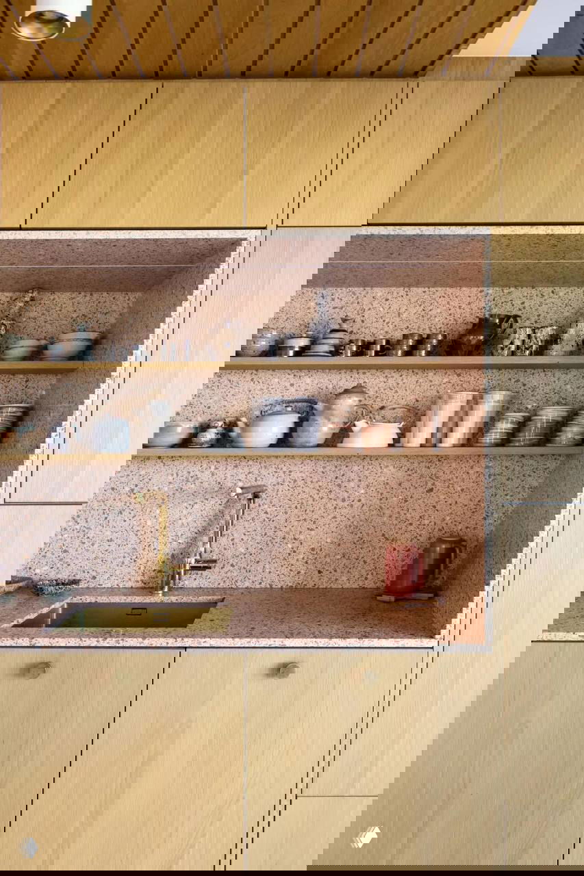 Кухонная ниша с терраццо-стеной и полками: светлая древесина шкафов и розоватая фактура рабочей поверхности.