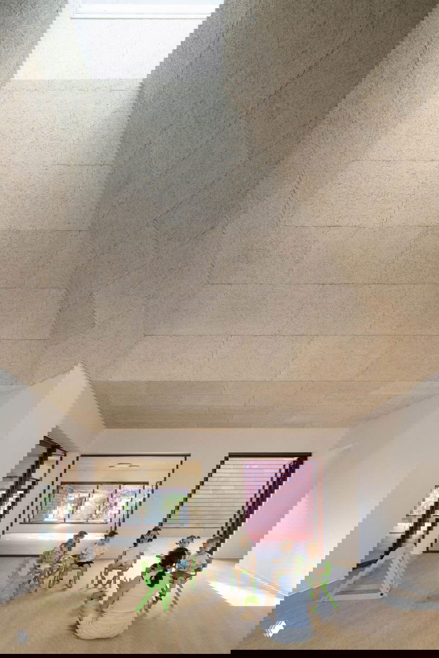 Учебный зал с белыми стенами, геометрическим световым отверстием в потолке и группой детей на полу — пример многофункциональной центральной площади