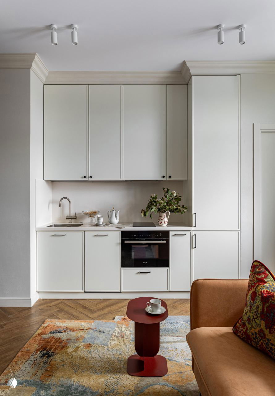 Кухня-гостиная в квартире 45 м² в стиле mid-century modern: белый кухонный гарнитур, терракотовый диван, горчичный столик и фактурный ковёр на деревянном полу.