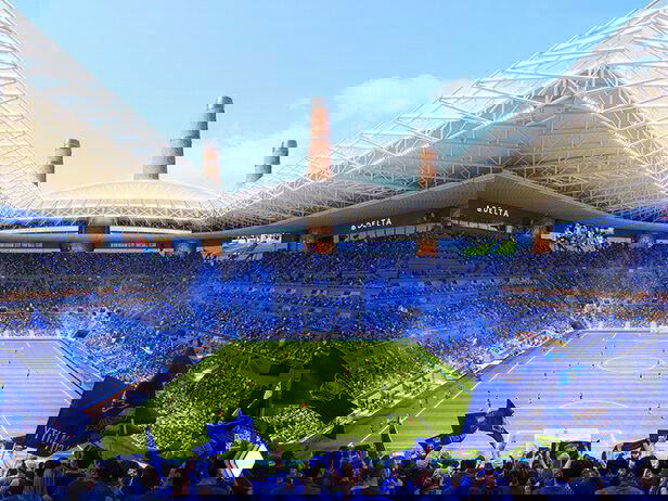 Интерьер трибун и поле стадиона во время матча, показывающий акустическую модель и атмосферу с болельщиками в синем.