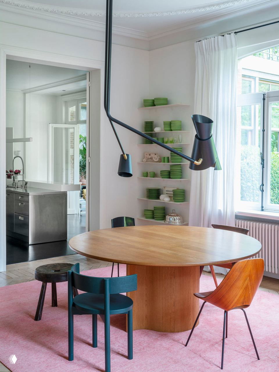 Столовая зона с круглым деревянным столом, разноцветными стульями, подвесной черной лампой и полукруглым окном, лёгкая и светлая атмосфера.
