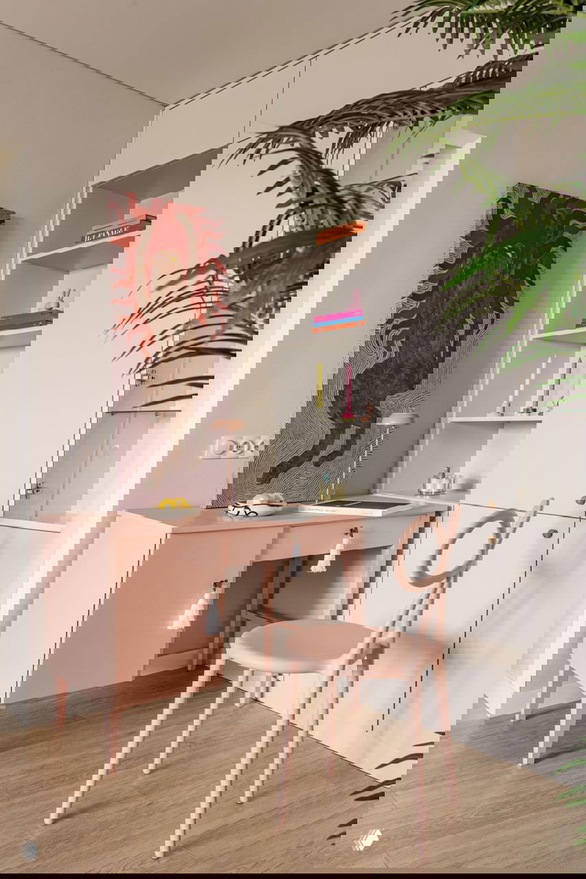 Рабочий уголок: розовый стол и изящный стул в стиле mid‑century, открытые полки с яркими книгами и свечами, лёгкий паркет и декоративные элементы в пастельных тонах.