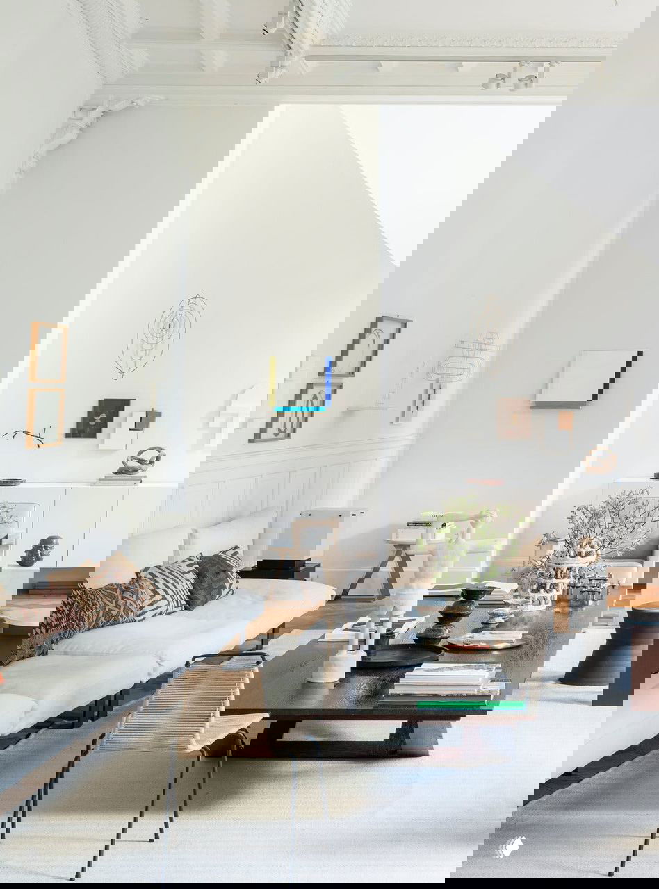 Просторная комната с длинным низким столом, диваном и настенной выставкой керамики и картин, интерьер в светлых тонах и художественные акценты.