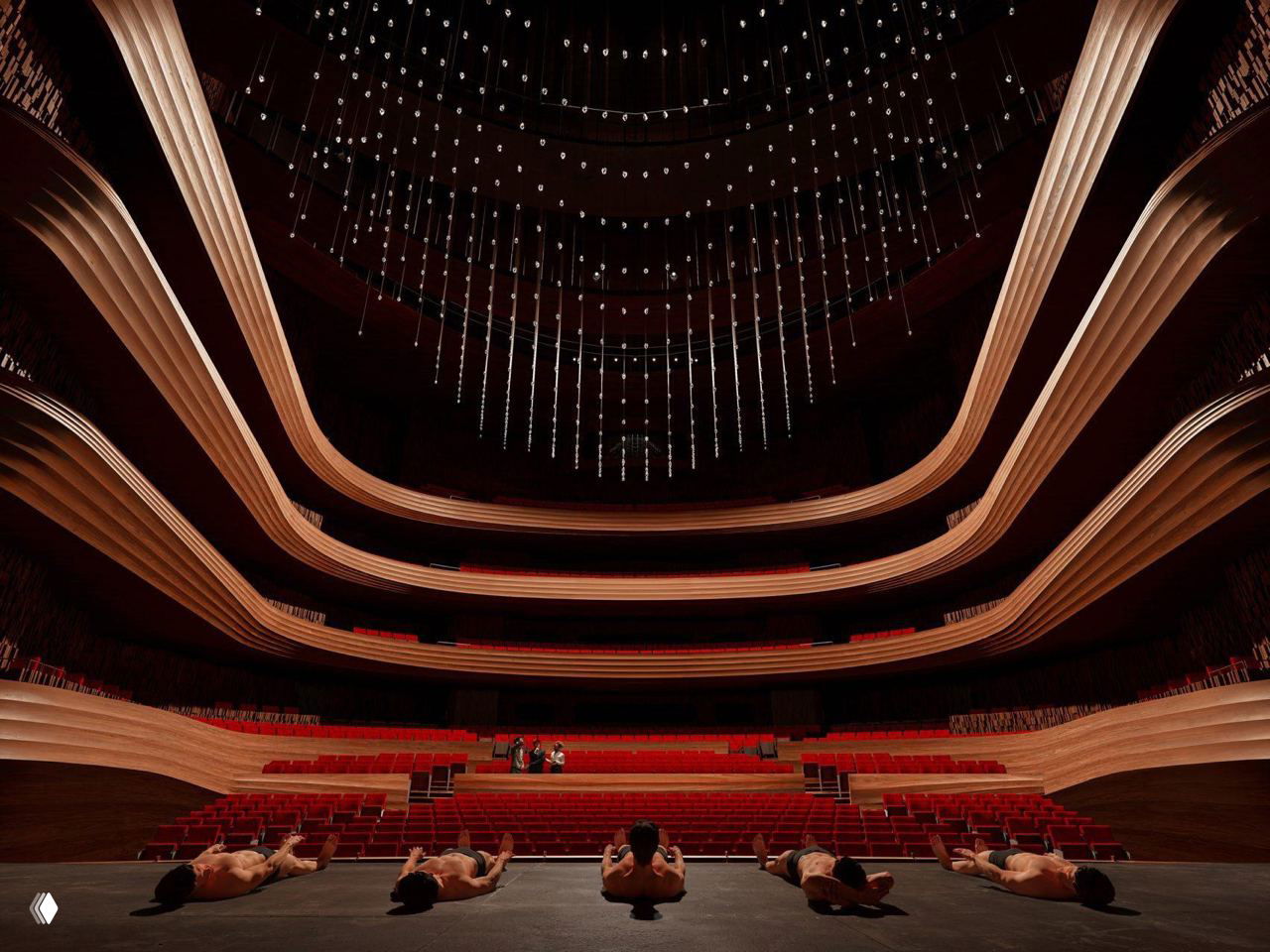 Зрительный зал оперы: три яруса балконов с волнообразными деревянными парапетами и подвесной световой инсталляцией над сценой.