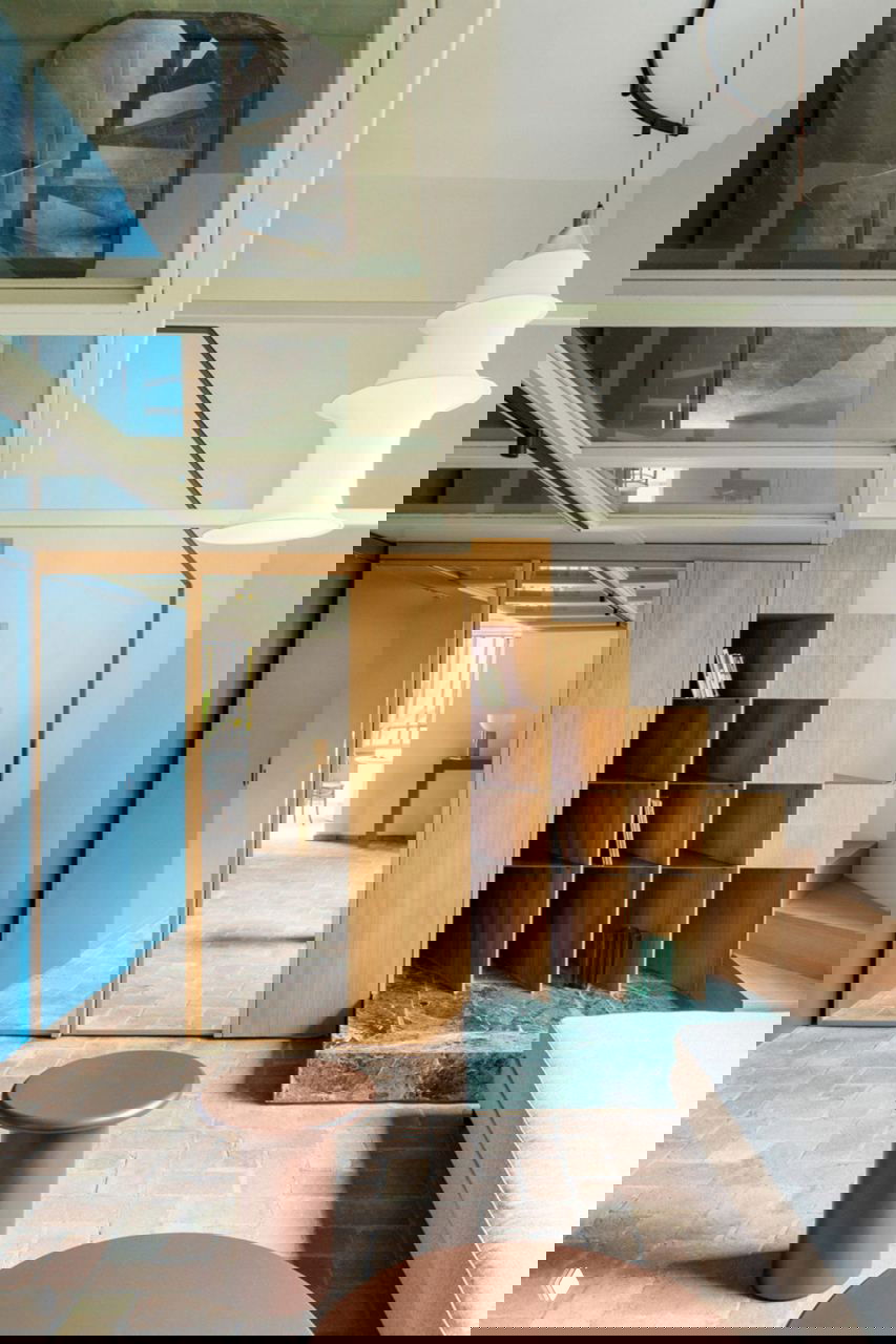 Интерьер: синий объём, модульная деревянная лестница‑стеллаж, зелёный мраморный подиум и фактурный терракотовый пол в гостиной.