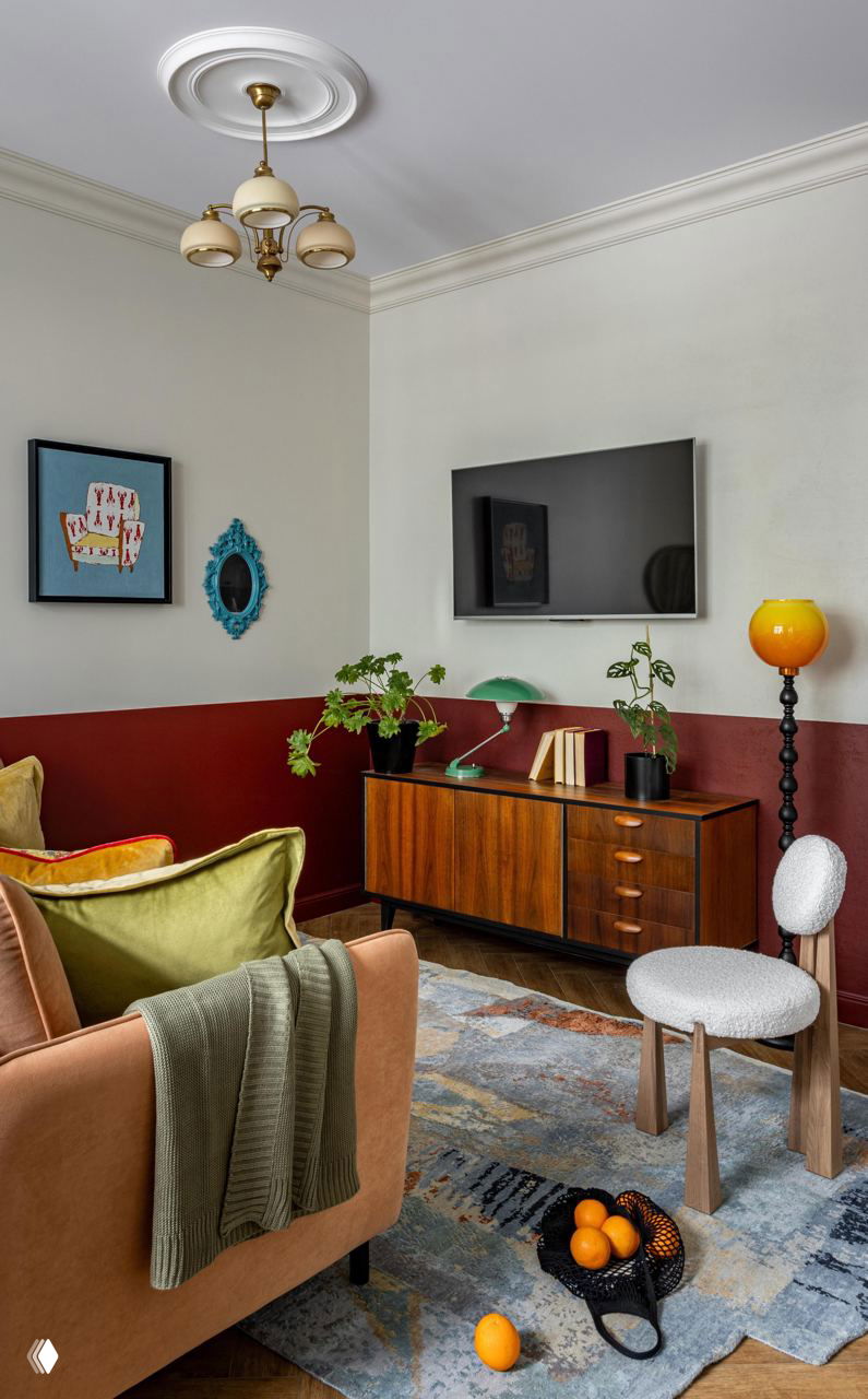 Интерьер гостиной с деревянной тумбой и лампой с жёлтым абажуром, бордовая отделка стен по низу и зелёные растения для живого акцента в композиции.