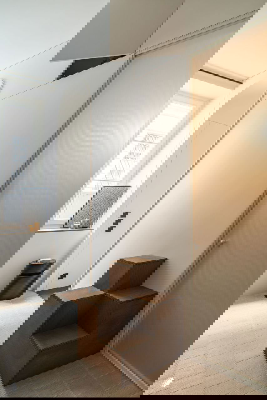 Деревянные модульные ступени и панельная перегородка, бежевый керамический пол и рассеянный дневной свет в минималистичном интерьере.