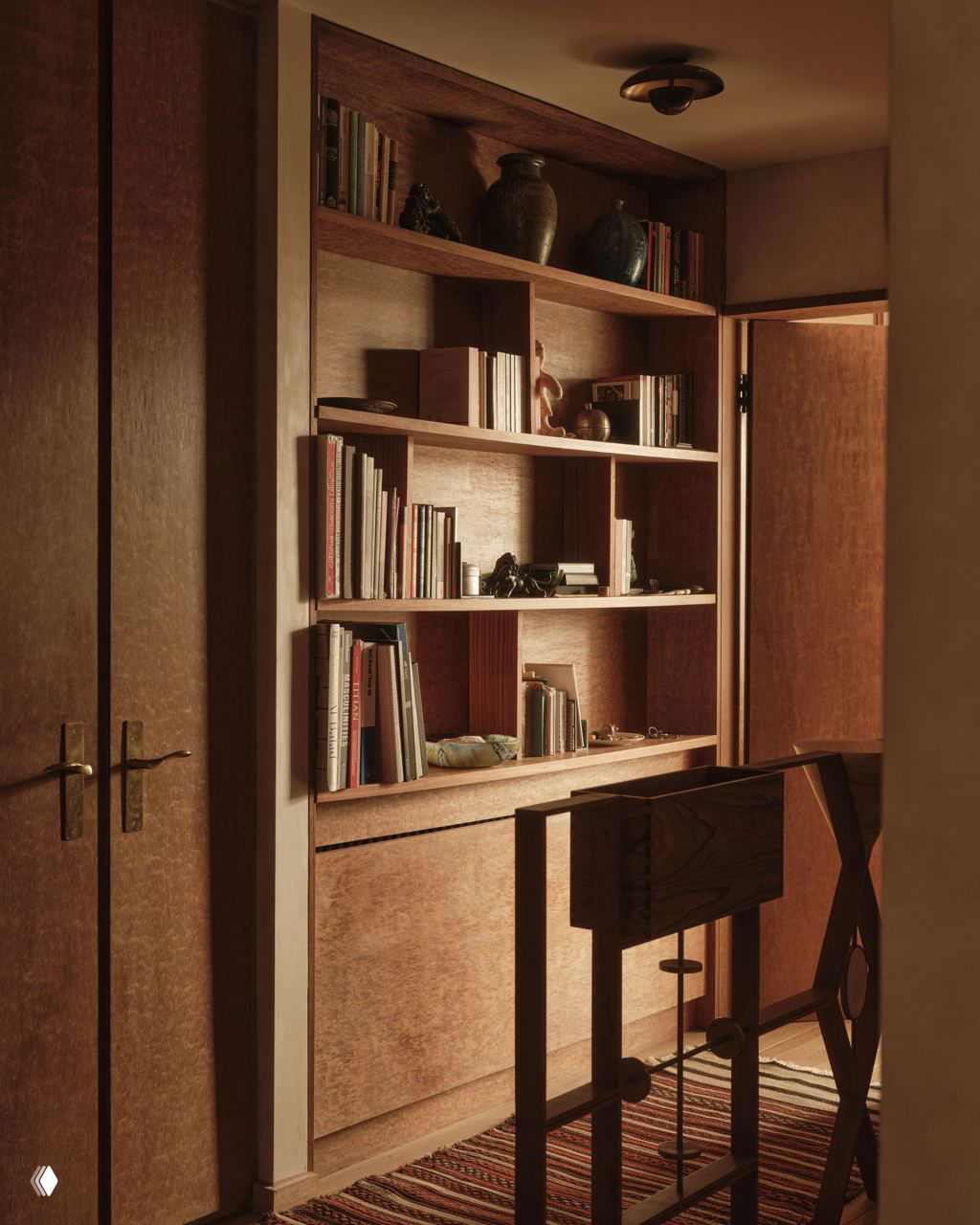 Ниша с открытыми деревянными полками, на которых стоят книги, керамика и вазы; тёплое боковое освещение подчёркивает текстуру дерева.