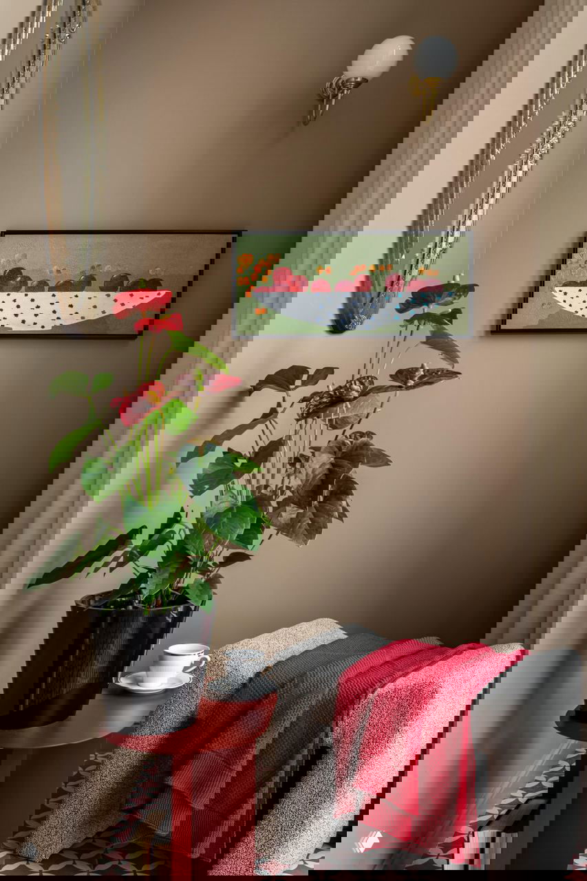 Уютный уголок с красно-горчичным столиком, растением в горшке и текстурным пуфом; картины и настенное зеркало добавляют глубины небольшой нише.