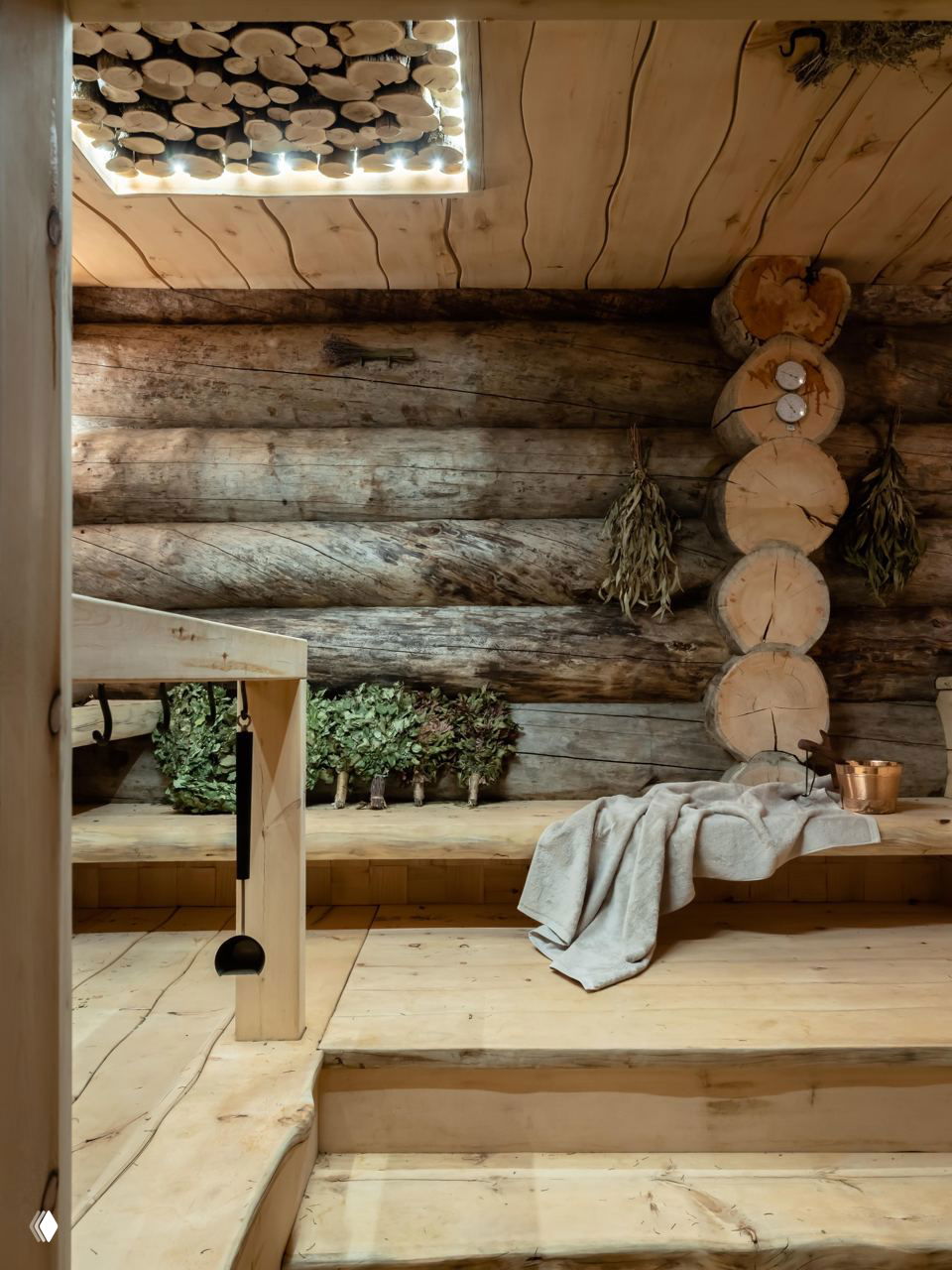 Интерьер русской бани в рустикальном стиле: массивные бревна стен, веники, простые деревянные скамьи и текстиль для отдыха.