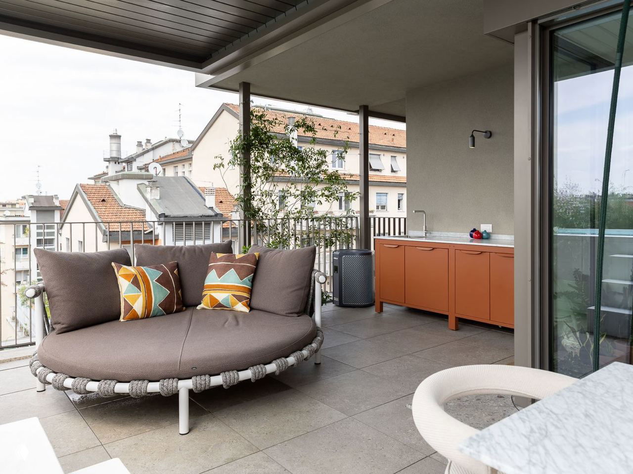 Балконная зона с круглым диваном-лежанкой, цветными декоративными подушками и видом на крыши миланских зданий — продолжение жилого пространства.