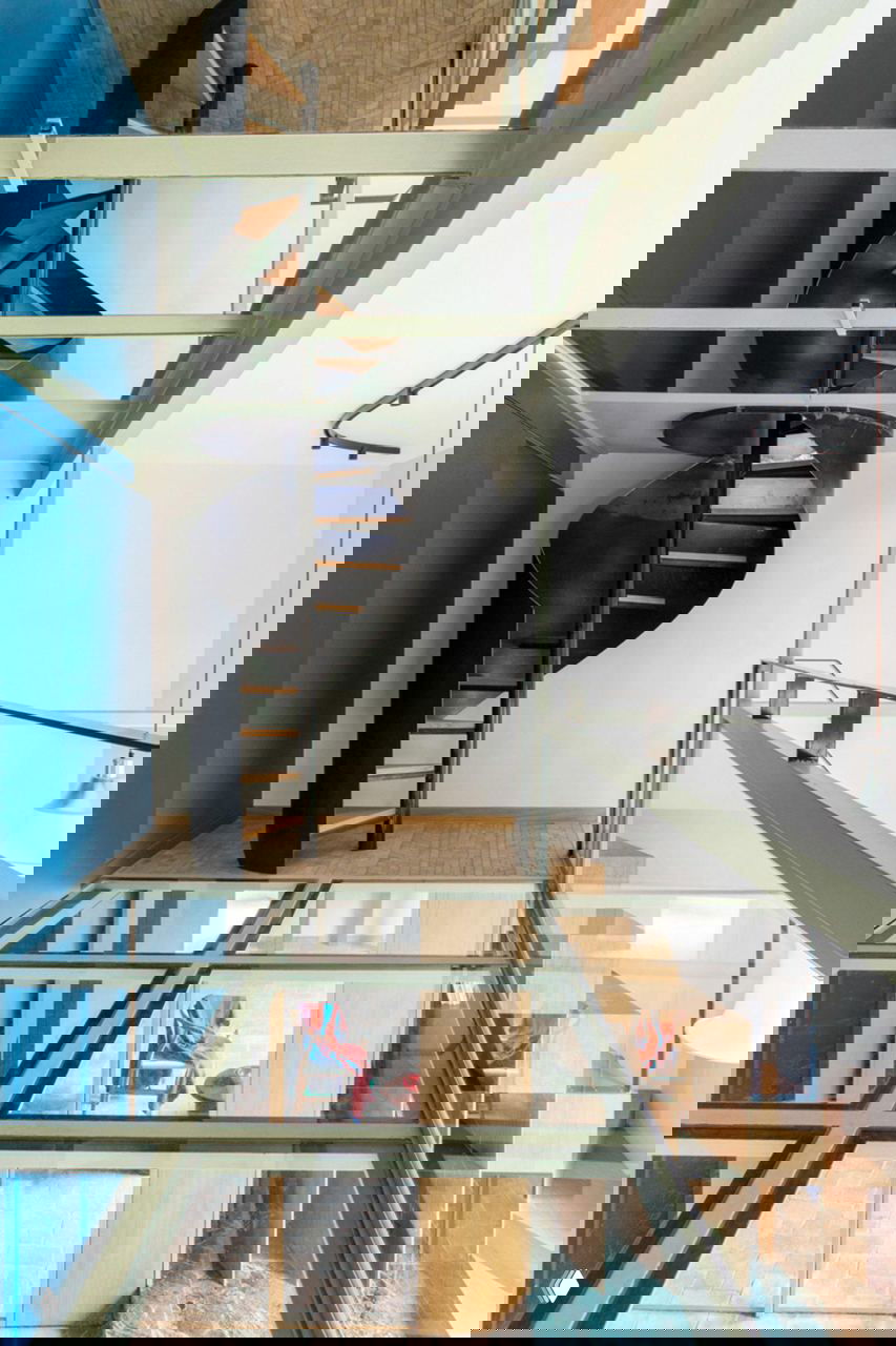 Винтовая скульптурная лестница и стеклянный настил между этажами: сочетание тёмного металла и прозрачных панелей в центре плана.