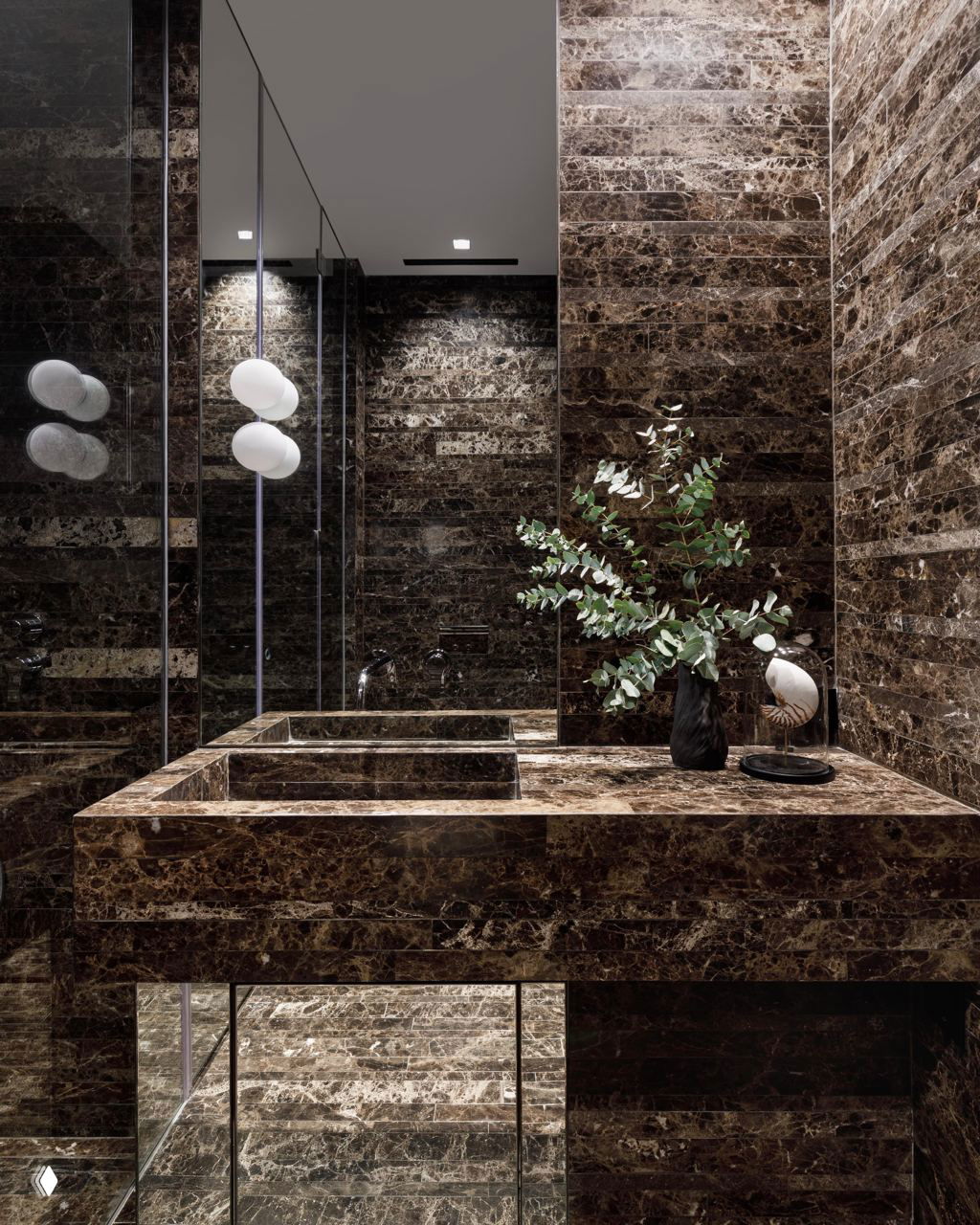 Тёмная ванная комната облицована коричневым мрамором, крупная раковина и отражающие поверхности создают дорогой и драматичный интерьерный образ.
