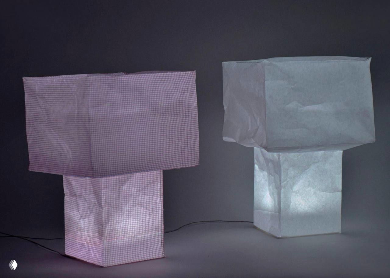 Включённые лампы Tsubomi вечером на тёмном фоне: розовая и серая версии излучают мягкий рассеянный свет, подчёркиваются тени и текстура складок в материале.