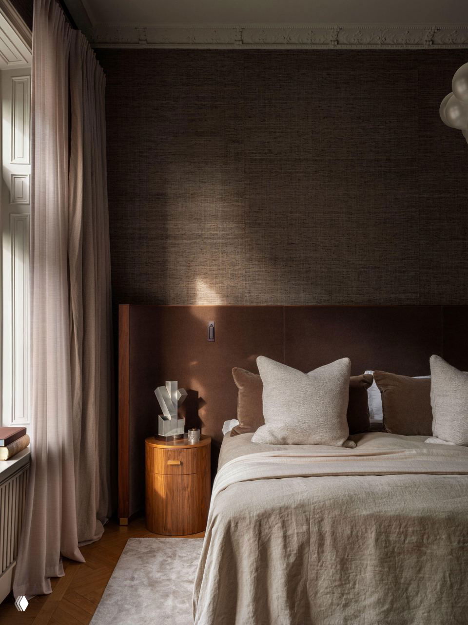 Спальня с тёплым кожаным изголовьем, нейтральными текстильными подушками и приглушёнными шелковыми обоями; на полу — классический паркет и светлый ковёр у кровати.