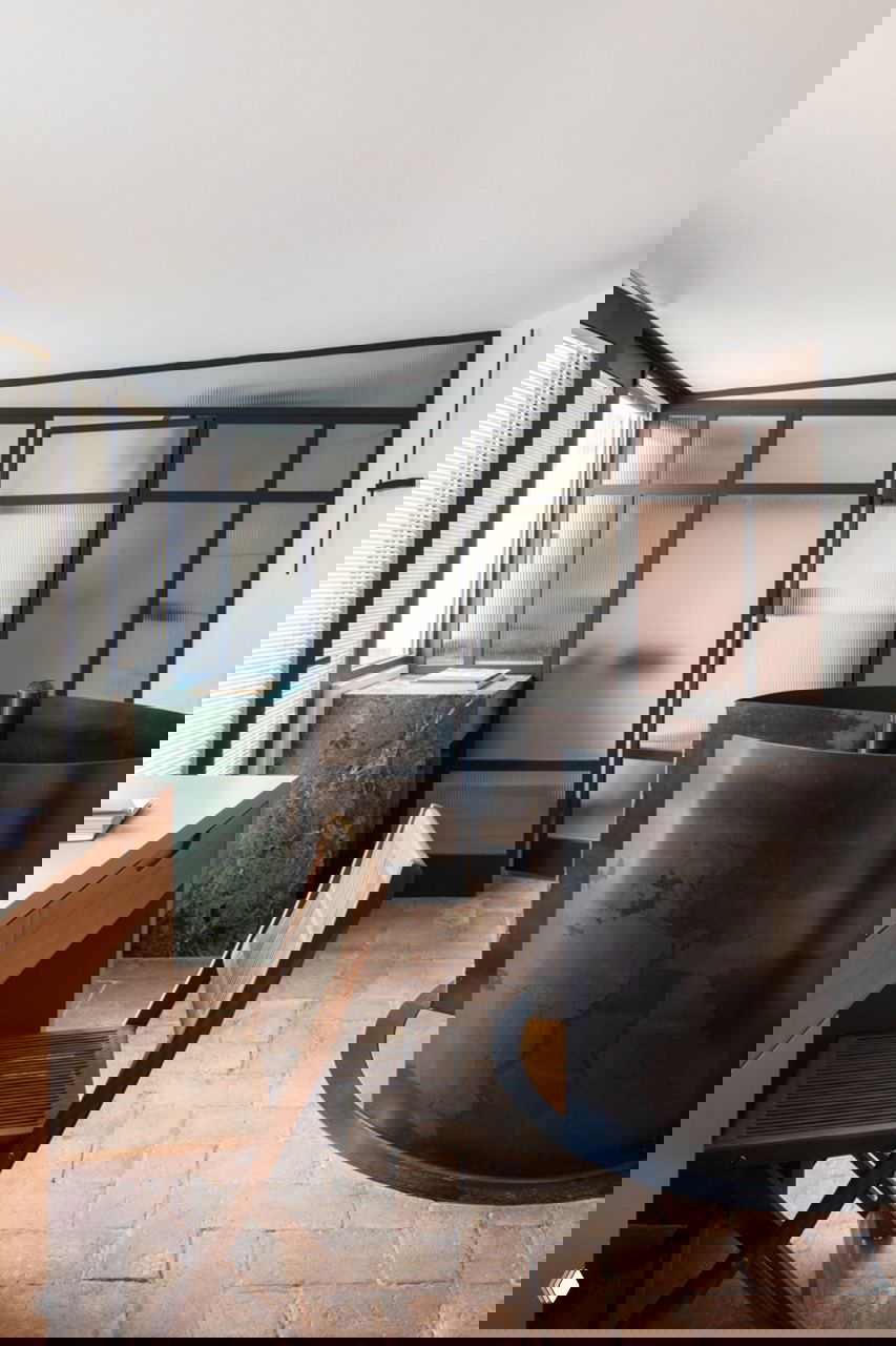 Рабочая зона и цилиндрическая конструкция с тёмным металлическим окрасом на фоне матовых стекол и мраморной столешницы в ванной/рабочем пространстве.